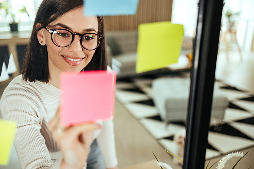 Businesswoman writing on colorful sticky note paper in business office