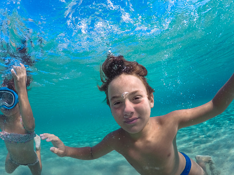 Boy looking at camera and having fun diving underwater on their summer vacation