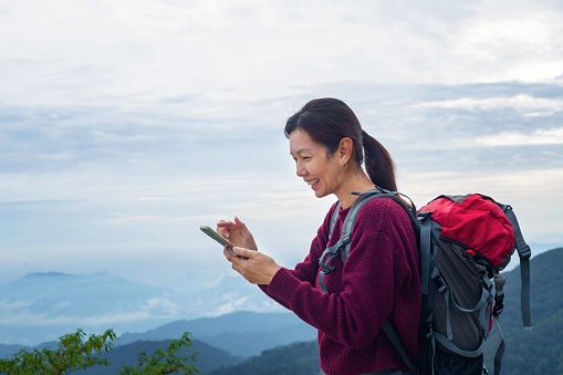Young female traveler relaxing and using a mobile phone while hiking with beautiful landscape