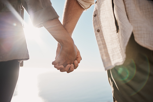 Love, unity and couple holding hands on the beach while on a date for romance or their anniversary. Trust, support and closeup of man and woman with hand intimacy and affection while on outdoor walk.