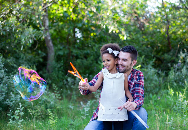 istock Happy father and daughter playing soap bubbles in park. 1492609432