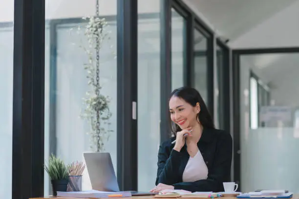 Photo of Woman's portrait in the office while working and researching ideas using a laptop. Happy businesswoman searches online for creative design, inspiration, and PPT review.