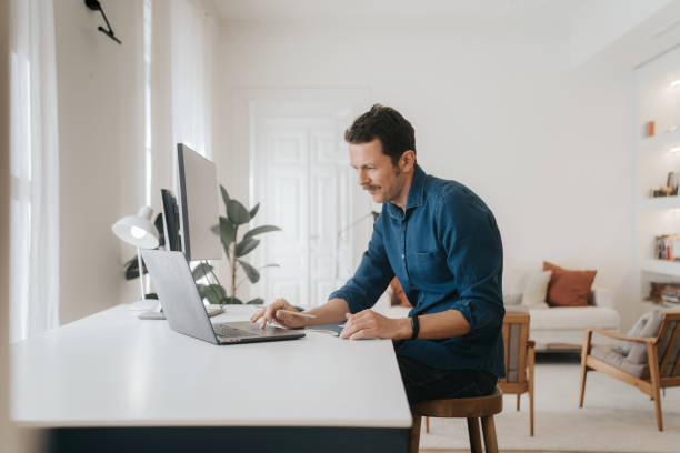 Homem sentado usando laptop em casa - foto de acervo