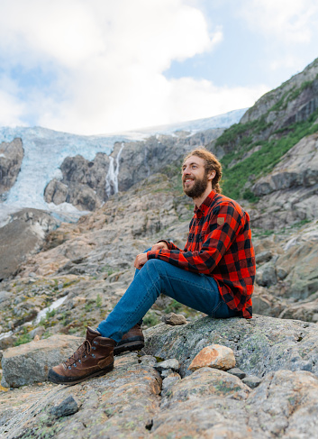 Young Caucasian man sitting on the background of Jostedalsbreen  glacier