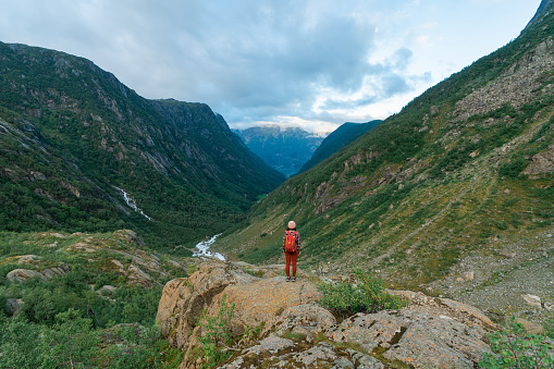 Young Caucasian woman standing on cliff and looking at river valley in Norway
