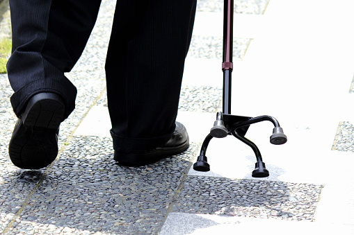 The feet of an old man enjoying a walk using a cane with a wide base and a sense of stability