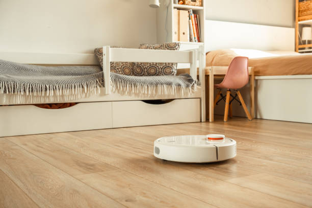 robotic vacuum cleaner working on laminate wood floor in the living room. automated white vacuum cleaner robot in the scandinavian interior designed house - appliance living room domestic room lifestyles imagens e fotografias de stock