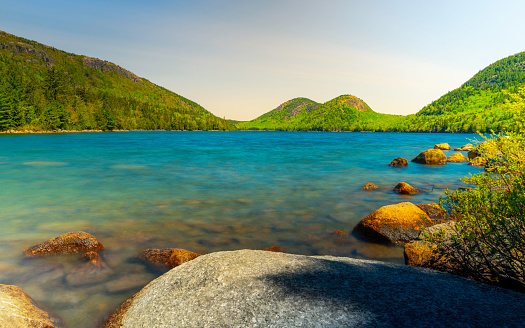 Tranquil Jordan Pond landscape in Mount Desert Island in Acadia National Park, Maine, vibrant spring green colors, gentle blue waves, and glacial rocks