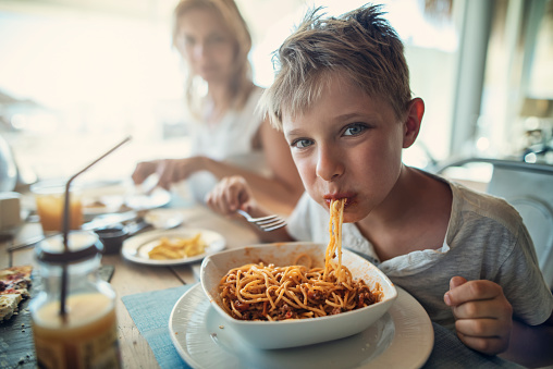 Mother and son enjoying meal in a restaurant. The boy is eating spaghetti and the mother is having a pizza.\nNikon D810