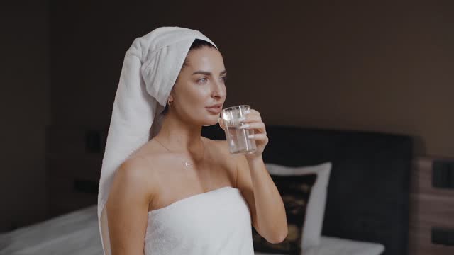 girl in towel on head standing and drink a glass of water