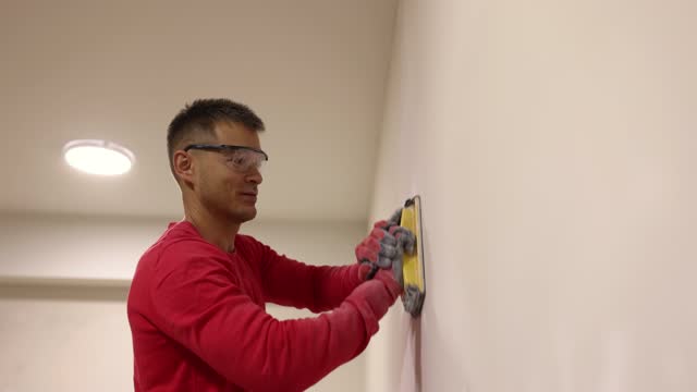 Positive worker polishes drywall with hand sander in room