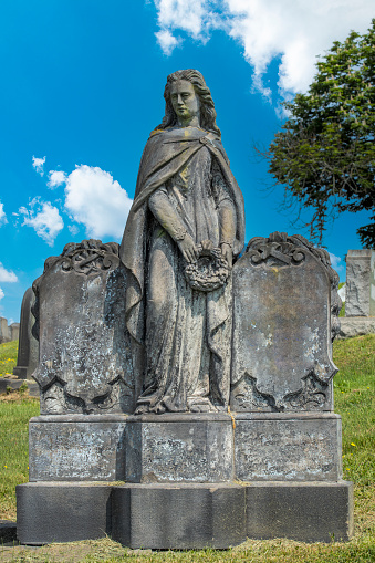 A tombstone from the 1800s with a full figure statue of a woman between two grave markers.