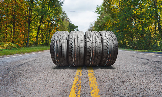 A summer sunny asphalt road through the forest with a new car tire set.