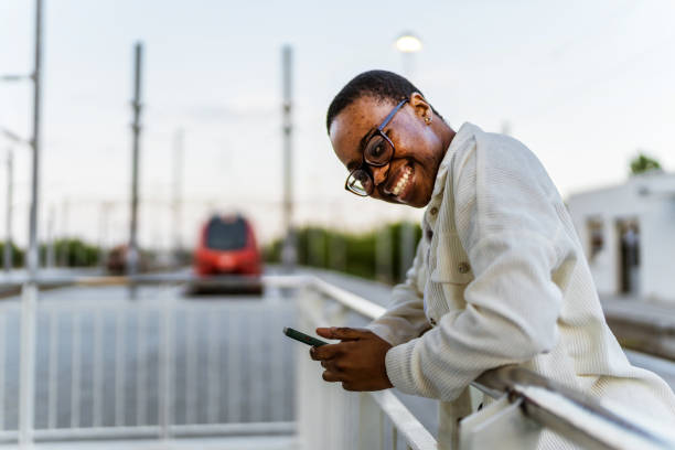 Young woman waiting for the train on station platform while using her smartphone during the day.