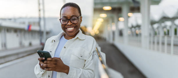 istock African woman waiting on train station and using smart phone during the day, looking at camera. 1492629169