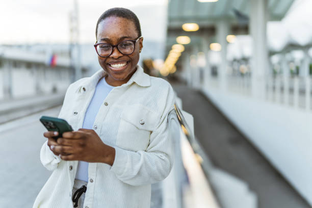 istock Young black woman waiting for the train on station platform and using smartphone. 1492629235