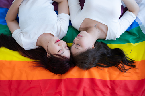 On a rainbow flag, an LGBT couples happily lie down, chatting, and teasing each other.
