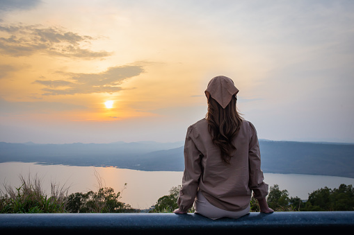 Woman sitting back looking at sunset with mountains and river in the background
