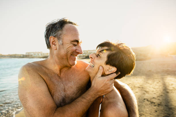 Happy senior couple having a romantic moment on the beach at sunset during summer vacations - Elderly people relationship concept stock photo