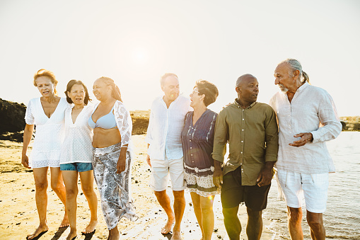 Happy multiracial senior friends having fun walking on the beach during summer holidays - Diverse elderly people enjoying vacations