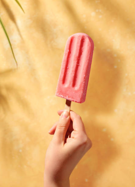 istock Woman hand holding pink fruit popsicle on sunny yellow background 1492637138