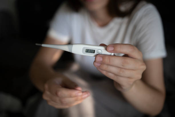 Woman suffering from a cold and flu takes her temperature with a thermometer