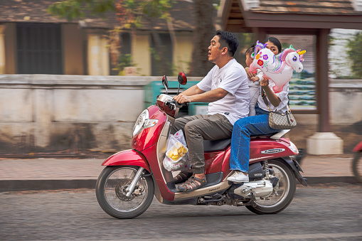 Luang Prabang, Laos - March 10th 2023: Family with one kid with a unicorn toy on a motorcycle in main street