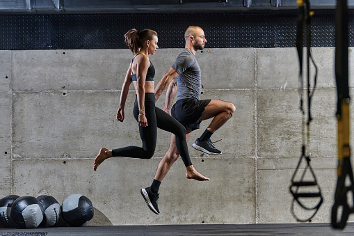 A fit couple exercising various types of jumps in a modern gym, demonstrating their physical fitness, strength, and athletic performance.