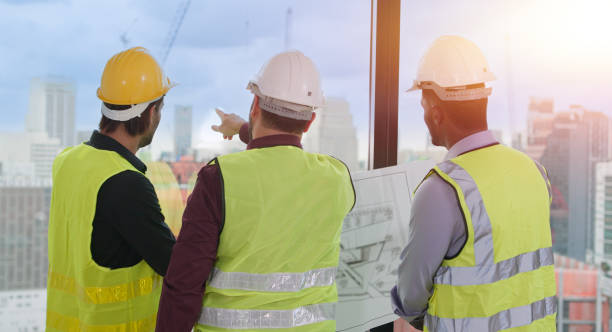 istock Back view, Team professional male civil engineer or Architect, inspector with contractor, foreman or worker. While look at blueprint plan inspect discuss meeting building project on construction site. 1492639351