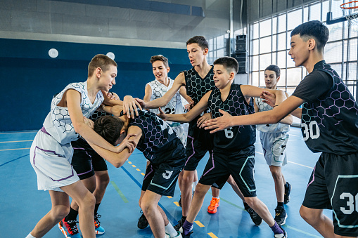 A team of male teenagers in an indoor basketball court, having a physical fight.