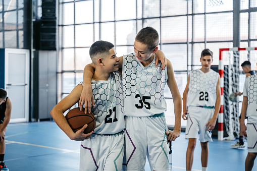Two male teenagers hugging after finishing a game in an indoor court.