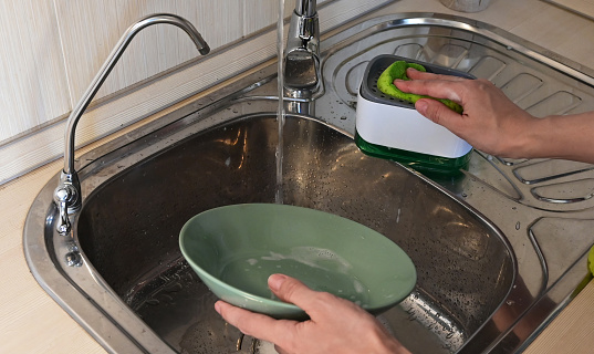 A woman washes dirty dishes with an eco-friendly detergent and a soap dispenser. House cleaning.