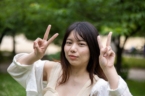 Portrait of young woman making a peace sign in public park