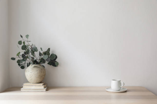 istock Minimal breakfast still life. Cup of coffee, tea. Empty white wall in sunlight table. Textured vase with silver eucalyptus leaves, branches on old books. Elegant Scandinavian working space, office 1492643045