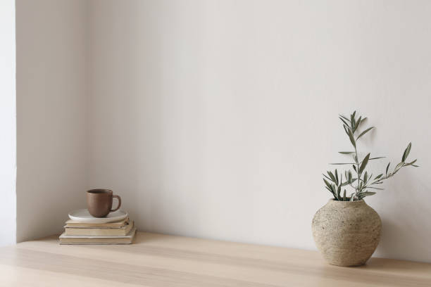 istock Neutral Mediterranean home design. Textured vase with olive tree branches, cup of coffee. Books on wooden table. Living room still life. Empty wall copy space. Modern interior, no people. Lateral view 1492643151