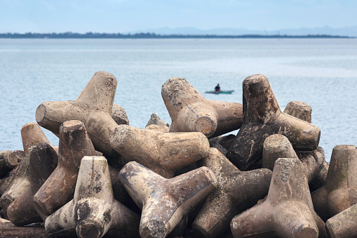 Tetrapods in a pile on the coast of Cebu Island in the Philippines. In the background is a fisherman in a small boat.