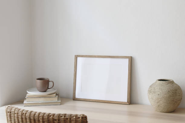 istock Empty horizontal picture frame mockup in minimalist interior. Wooden table, blurred rattan chair. Vase with cup of coffee. White wall background. Landscape template of artwork, painting, poster. 1492643246