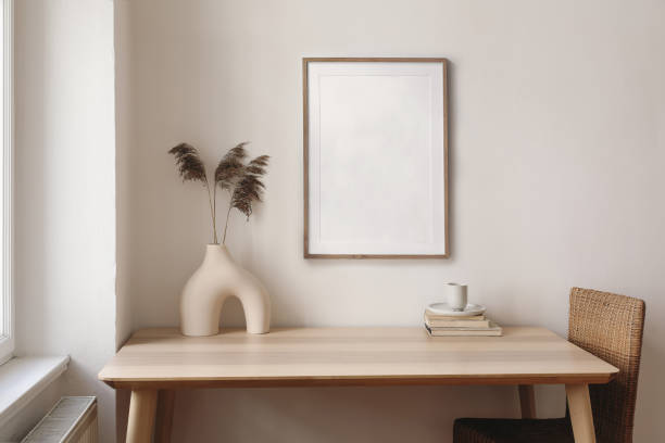 istock Decorative boho still life. Modern vase with dry reed, grass on table, desk. Empty wooden picture frame mockup. Cup of coffee, books and rattan chair. Artistic poster display. Elegant home interior. 1492643281
