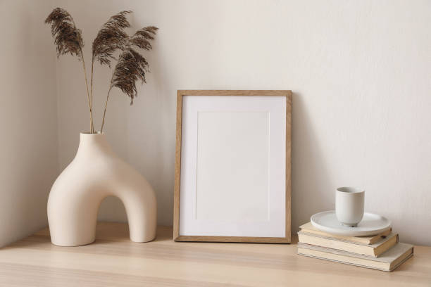 istock Blank wooden vertical picture frame mockup. Vase with dry reed, grass on table, desk. Cup of coffee, books. Elegant interior, home office. Decorative boho still life photo. Artistic poster display. 1492643377