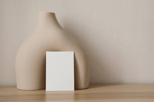 Modern wedding stationery. Closeup of blank greeting card, invitation mockup. Beige boho ceramic vase, geometric sculpture. Contemporary neutral branding still life. Trendy boho style, modern organic shape papelería de boda moderna. primer plano de una tarjeta de felicitación en blanco, maqueta de invitación. jarrón de cerámica boho beige, escultura geométrica. bodegón contemporáneo de marca neutra. estilo boho de moda. forma orgánica moderna