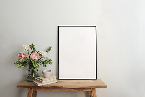 Blank black picture frame mockup. Artistic table, wooden bench still life composition with cup of coffee, old books. Spring bouquett of pink tulips, white daffodils, hawthorn, guelder rose flowers.