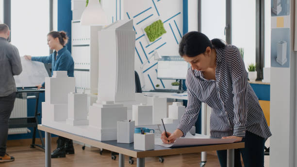 istock Woman architect analyzing blueprints plan on table to design building model and maquette 1492651495