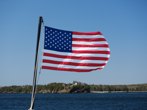 The American flag flies off the back of the Vinalhaven ferry with the Owls Head lighthouse on the cliffs in the background