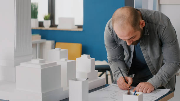 istock Close up of architect taking notes on blueprints plan to work on building model and maquette 1492651552