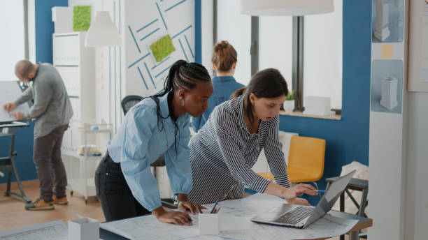 istock Team of diverse women using laptop to design blueprints plans for building construction on table 1492651908