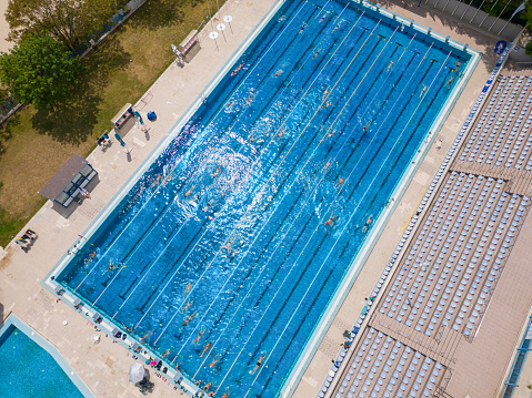 The open sports swimming pool glistened under the bright sun as people swimming in its inviting waters. Their synchronized strokes created a vibrant tapestry of movement, while the pool's blue expanse mirrored the joy and energy.