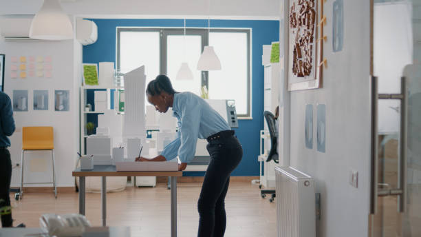 istock Woman architect working on blueprints plan to design construction layout with building model 1492652709