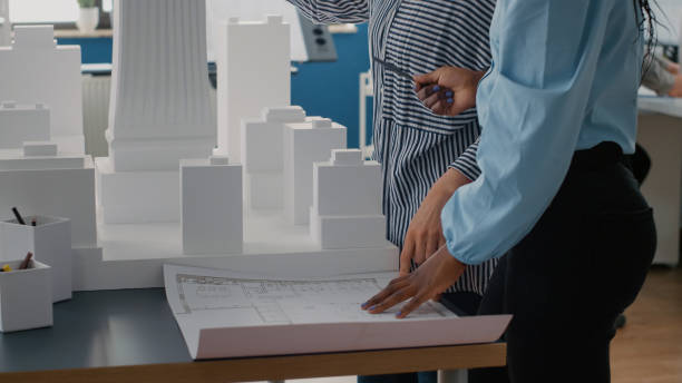 istock Close up of architects placing blueprints plan on table to work on urban project with building model 1492653294
