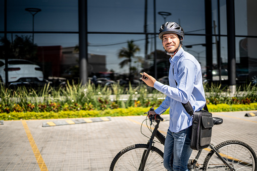 Young man walking with bicycle and using mobile phone outdoors