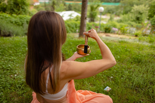 Female yogi is using rin gong to connect with her self in a beautiful green landscape.